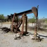 Over-exploitation of Mineral Resources and Conservation for Primary 6 3 Abandoned rusty oil pumpjack in a barren desert landscape under clear blue skies.
